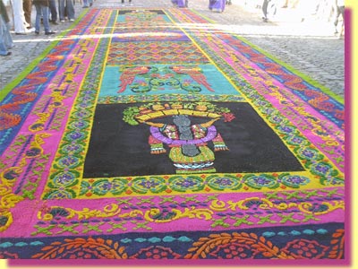 Another Calle Ancha carpet with a Mayan theme .. an Mayan in the foreground holds pineapples and fruits on her head and beyond her a guacamayas, big macaws ... click to see a large image